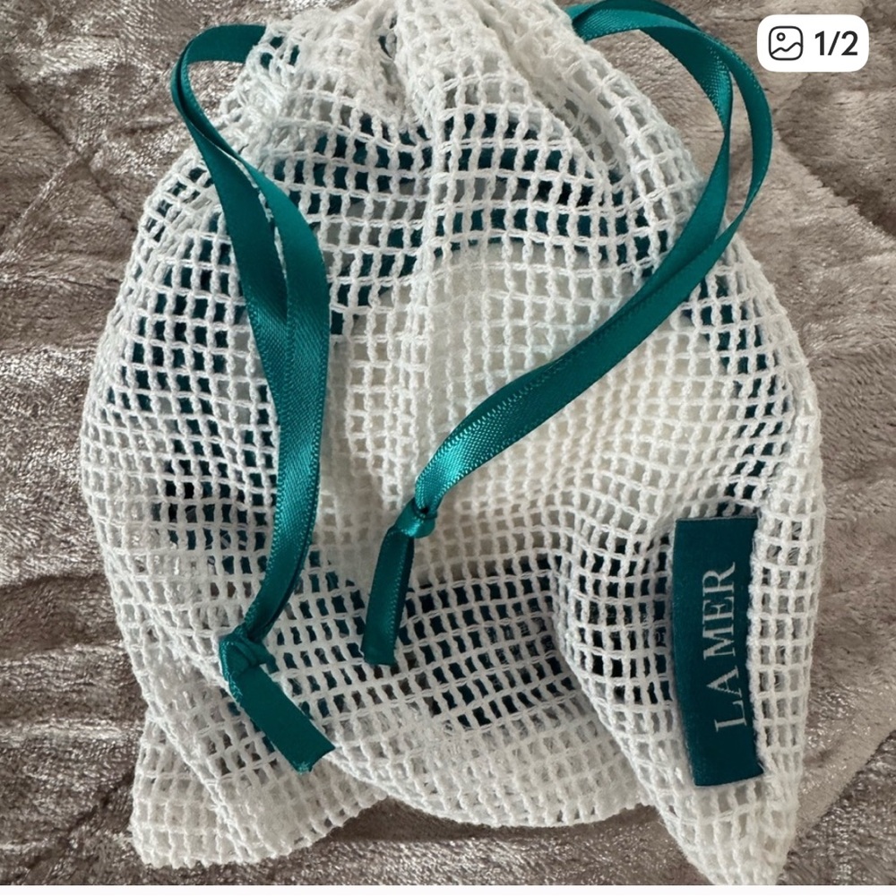 La Mer White Mesh Pouch with Teal Ribbon contains 3 reusable cleansing pad.